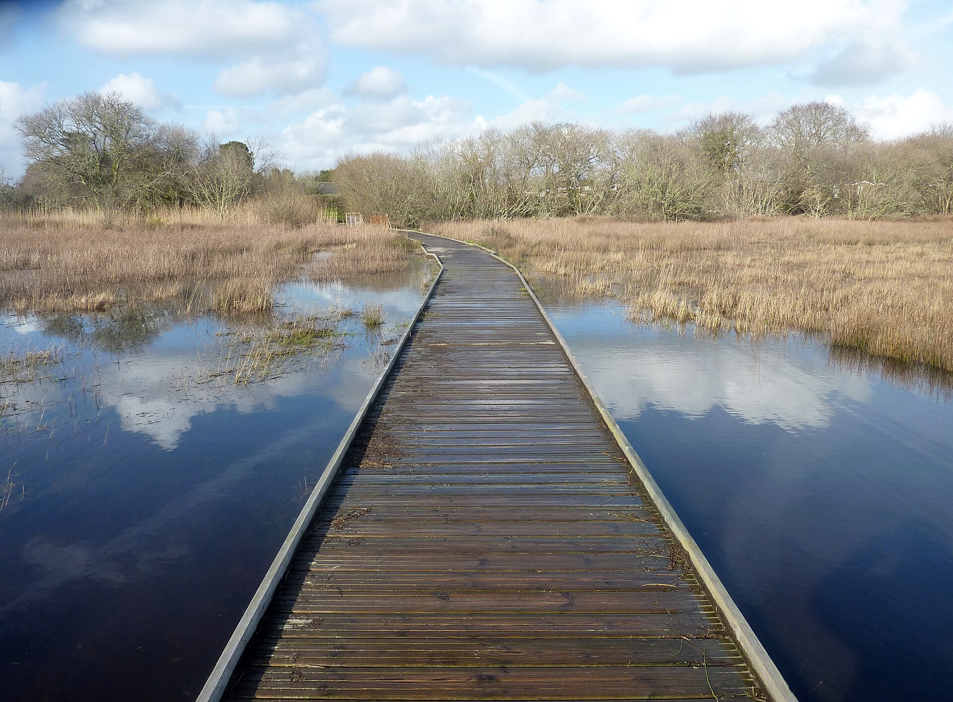 Passerelle en bois traversant le marais de Mousterlin inondé, reflets du ciel